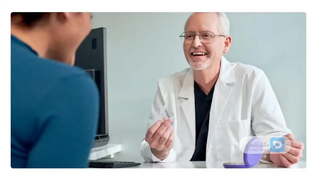 یک دکتر ارتودنسی که قالب ارتودنسی شفاف را در دست دارد و در حال توضیح دادن به بیمار خود است